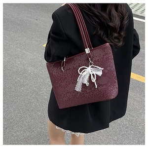 Detail of burgundy snakeskin tote bag featuring lace bow and pearl heart charm accessory