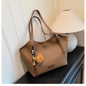 Macro detail of brown litchi pattern leather tote bag with cute bear charm and logo