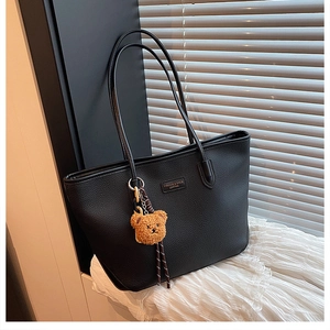 Dettaglio borsa tote nera in pelle martellata con logo in metallo e ciondolo orsetto