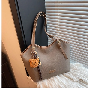 Detail of beige pebble leather tote bag with long strap and cute brown plush bear charm