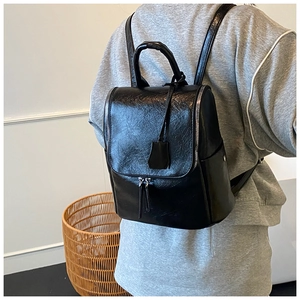 Rear view of model wearing a black glossy leather fashion backpack with dual zip details