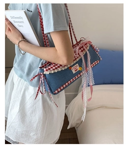 Detail of blue denim baguette bag with red gingham trim and cherry patch on shoulder