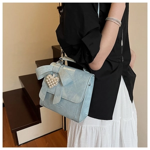 Detail of light blue bow handbag with a white pearl heart charm on textured leather