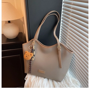Close-up of litchi grain tote bag with fashion tag and cute plush bear charm detail