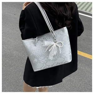 Detail of silver snake-pattern tote bag featuring a pearl lace bow charm on shoulder strap