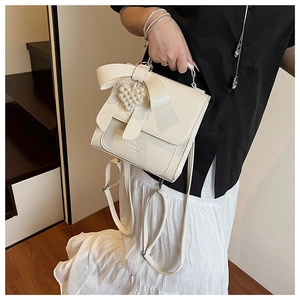 Detailed view of cream bow handbag featuring a pearl heart charm and metallic silver clasp