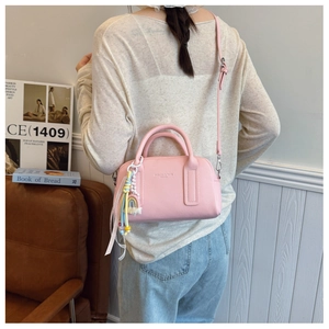 Pink lychee leather crossbody bag with a rainbow tassel charm on a model's back