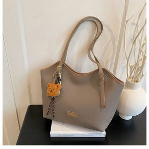 Detail of taupe pebbled leather tote bag with adjustable handles and plush bear charm