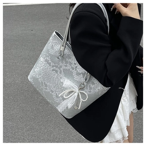 Close-up of silver tote bag featuring snake pattern texture and pearl lace bow charm