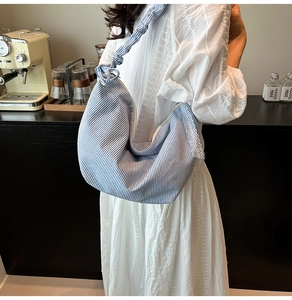 Detailed close-up of blue striped dumpling bag with knot shoulder strap and lace trim