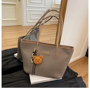 Dettaglio di una grande borsa tote grigia con un ciondolo a orsetto di peluche e logo in metallo