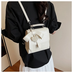 Chic cream bow backpack shown on model with pearl heart charm and textured finish