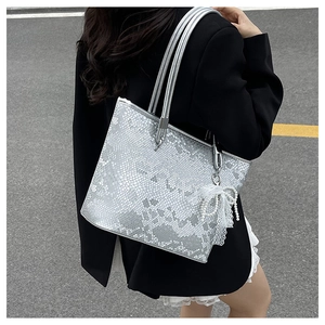 Detailed close-up of a silver snakeskin tote bag with pearl lace bow charm accent