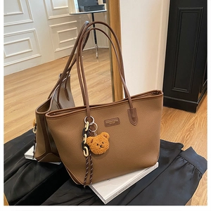 Dettaglio borsa tote marrone motivo litchi con ciondolo a orsetto e etichetta moda