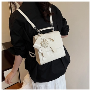 Detail of cream-colored patent leather backpack featuring a large bow and pearl heart charm