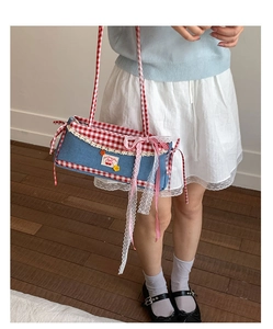 Detail of denim baguette bag with red gingham trim, lace lace, and pink ribbon bow