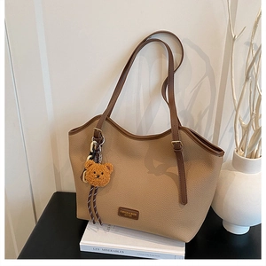 Close-up of litchi pattern leather tote with a brown plush bear charm and fashion label
