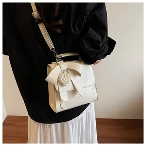 Detail of cream white PU leather bag with large bow and pearl heart charm accessory