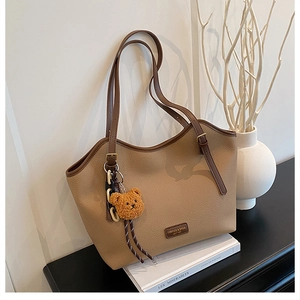 Detail of coffee brown litchi pattern tote bag with teddy bear charm and leather label