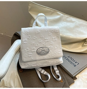 Detail von weißem Jacquard-Stoff mit Blumenrelief und silbernem Logo auf dem Rucksack