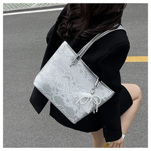 Detail of silver snake-pattern tote bag with white lace bow and pearl charm accessory