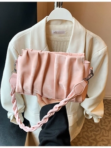 Pink pleated crossbody bag with woven strap detail shown against a beige blazer
