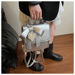 Detail of silver metallic textured backpack with bow and pearl heart charm accessory