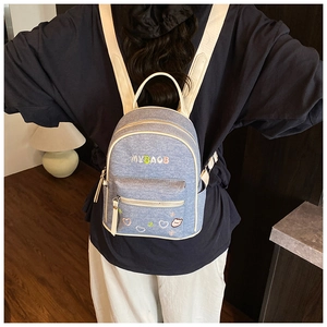 Detail of light blue denim mini backpack with white trim and cute embroidery on a model