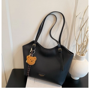 Detail of black pebbled leather tote bag with adjustable straps and bear charm