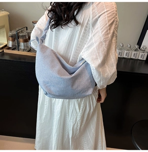 Blue and white striped canvas hobo bag worn by a model on a shoulder with a wide strap