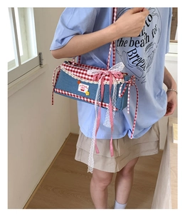 Close-up of denim shoulder bag with red gingham trim and cherry appliqué detail