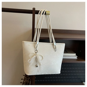 Close-up of white snake-embossed tote bag featuring pearl lace bow and rope straps