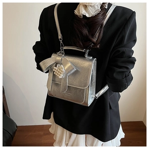 Detail of silver metallic textured backpack with bow and pearl heart charm on model