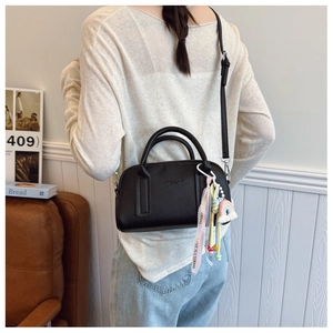 Detail of black pebbled leather crossbody bag with rainbow charm and decorative strap