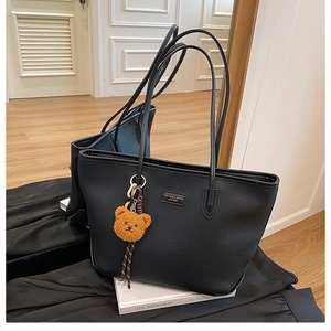 Dettaglio della borsa tote in pelle martellata nera con spalline sottili e ciondolo orso
