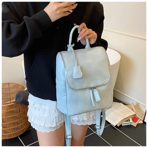 Close-up of a light blue leather fashion backpack featuring a stylish top handle and charm