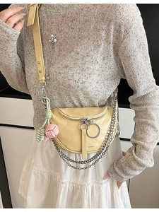 Yellow quilted saddle crossbody bag with metal chain strap and woven ball charm on a model
