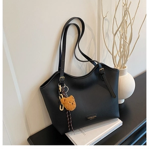 Detail of black pebbled leather tote bag with gold metal plaque and plush bear charm