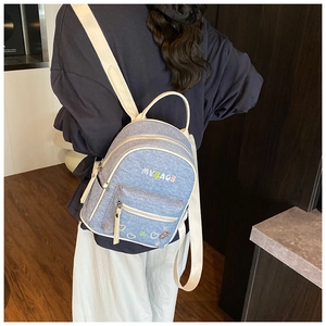 Detailed close-up of blue denim backpack featuring vibrant embroidery and white canvas straps