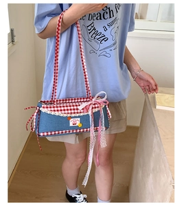 Detail of blue denim shoulder bag with red gingham trim and cherry embroidery