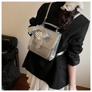 Detailed back view of a metallic silver backpack with a bow and pearl heart pendant