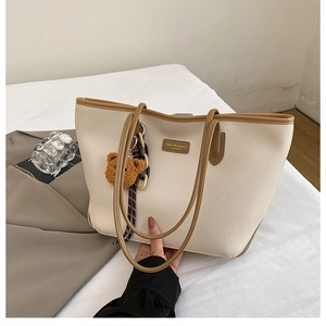 Dettaglio della borsa tote beige con finiture in pelle marrone e ciondolo a forma di orsetto