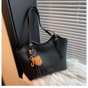 Detail of black pebbled leather tote bag featuring a cute bear charm and golden hardware