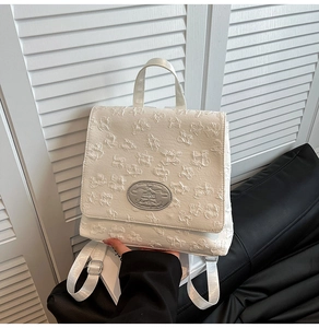 Details des weißen Rucksacks mit Blumenprägung und silbernem Logo-Schild