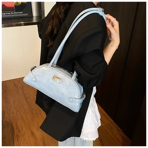 Detail showing light blue faux crocodile texture and metal plaque on the underarm bag