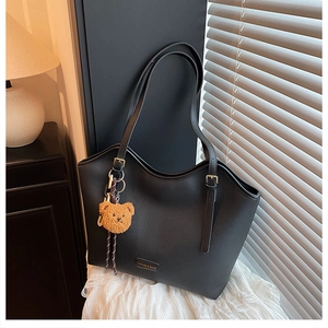 Detail of black pebbled leather tote bag with thin straps and cute brown bear pendant