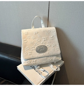 Detailaufnahme der geprägten Blumustextur und des silbernen Logos auf dem weißen Rucksack