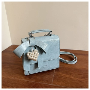 Detailed view of light blue glossy bow bag featuring a heart pearl pendant accessory