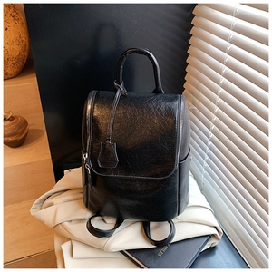 Detail of black vintage cracked leather backpack showing texture and hand strap in sunlight