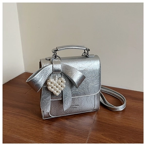 Detail of silver metallic textured crossbody bag with oversized bow and pearl heart charm